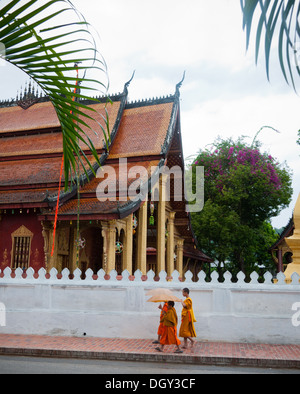 A group of three (3) Buddhist monks walk by Wat Sen Buddhist temple in Luang Prabang, Laos. Stock Photo