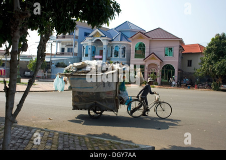 A man who collects recyclable material is walking with his bicycle and homemade cart on a city street in Kampong Cham, Cambodia. Stock Photo