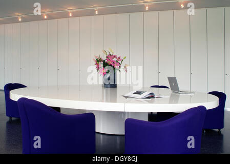 Oval conference table with a laptop and chairs in a modern design in front of a white office wall unit Stock Photo