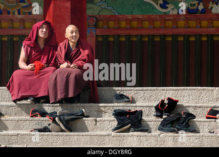 Tibetan monks wearing robes of the Gelug or Gelug-pa Order sitting beside their removed boots in front of the Assembly Hall Stock Photo