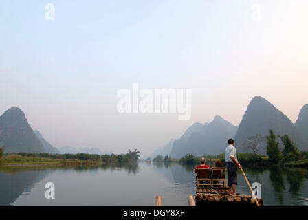 Bamboo raft with tourists and Chinese man on the Yulong River in the rocky karst landscape near Yangshuo, Guilin, Guangxi, China Stock Photo