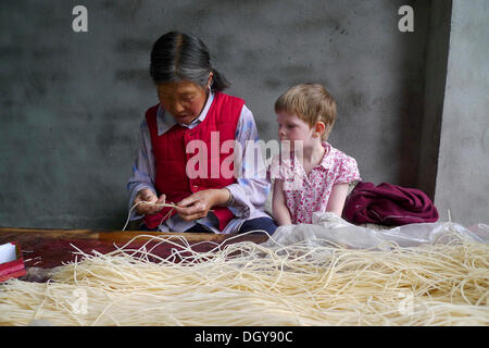 Encounters in China, young European girl watching on old Chinese woman making incense sticks, Moxi, Hailuogou, Sichuan, China Stock Photo
