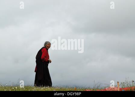 Elderly Tibetan woman wearing a traditional Tibetan costume, walking on a Kora pilgrimage in the grasslands of Tagong near the Stock Photo