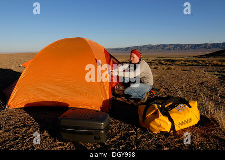 Young woman setting up camp with orange trekking tent and outdoor equipment in the Gobi Desert, Khorgoryn Els Stock Photo