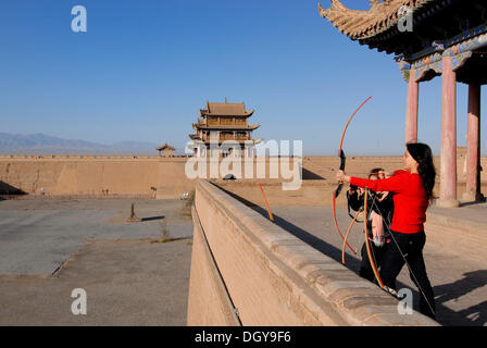 Chinese woman using a bow and arrow at the Jiayuguan Fortress with two gatehouses at the western end of the Great Wall of China Stock Photo