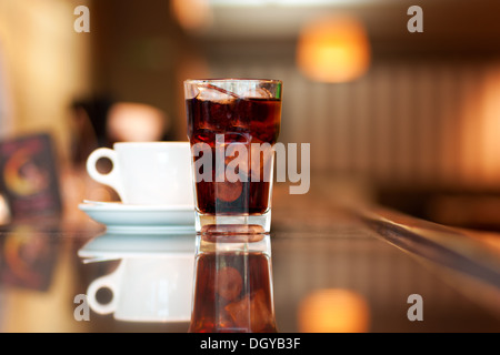 A glass of cola or soda with ice cubes and cup of black coffee on the bar Stock Photo