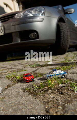 A toy car crash with a toy police car, real car in background Stock Photo