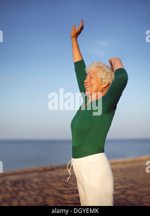 Senior woman stretching on the sandy beach. Mature caucasian woman exercising by the sea.