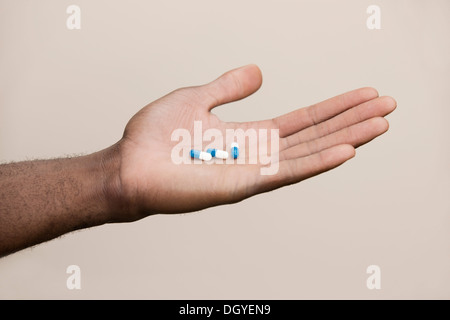 Man holding out three drug capsules Stock Photo