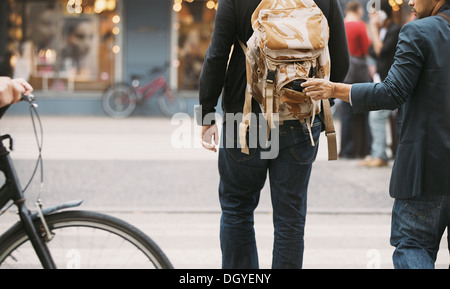 Thief stealing wallet from backpack of a man walking on street during daytime. Pickpocketing on the street during daytime Stock Photo