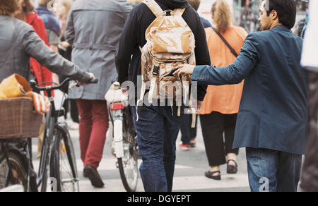 Young man taking wallet from backpack of a man walking on street during daytime. Pickpocketing on the street during daytime Stock Photo