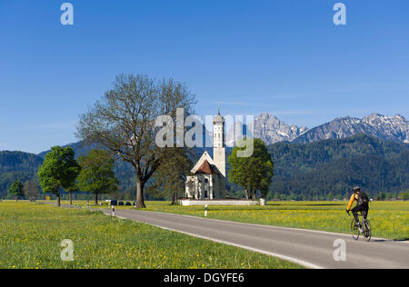 Cyclist on the road to the pilgrimage church of St. Coloman, Schwangau near Fuessen, Bavarian Alps, Allgaeu, Upper Bavaria Stock Photo