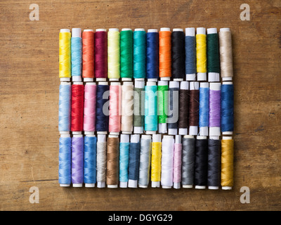 Rows of various colored spools of thread on a wooden table Stock Photo