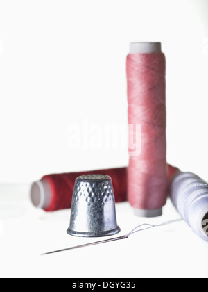 A shiny thimble and threaded needle with three spools of thread Stock Photo