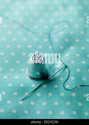 A threaded needle and thimble on top of polka dotted fabric Stock Photo