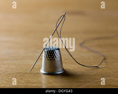 A threaded needle balanced against a shiny metal thimble Stock Photo