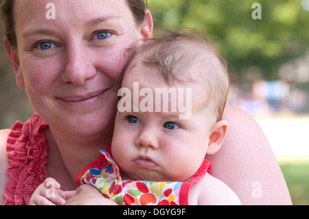 Close up of mother cuddling her baby girl outside in the garden Stock Photo