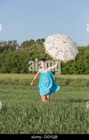 A young girl holding an umbrella up while running through a field in summer Stock Photo