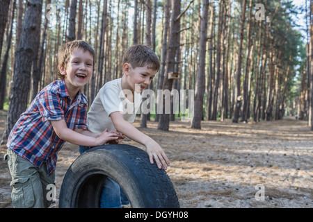 Two young boys pushing a tire in a wooded area Stock Photo