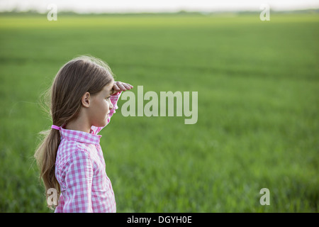A young girl standing in a field, shielding her eyes and looking at view Stock Photo