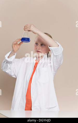 A girl wearing a lab coat and holding a conical flask with blue liquid in it Stock Photo