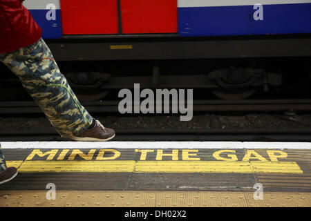 Yellow marking MIND THE GAP on the floor of a station of the London Underground, a person wearing military pants taking a step Stock Photo