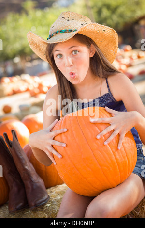 Preteen Girl Holding A Large Pumpkin at the Pumpkin Patch in a Rustic Setting. Stock Photo