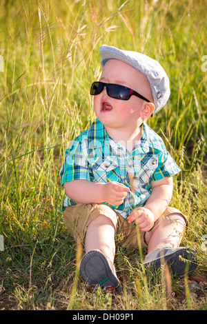 Young toddler boy with sunglasses sitting in tall grass crying. Stock Photo