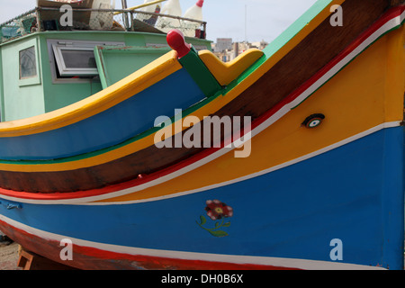 A traditional Maltese fishing boat, the Luzzu hauled up and being repainted on the harbour side Stock Photo