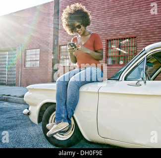 Mixed race woman sitting on vintage car Stock Photo