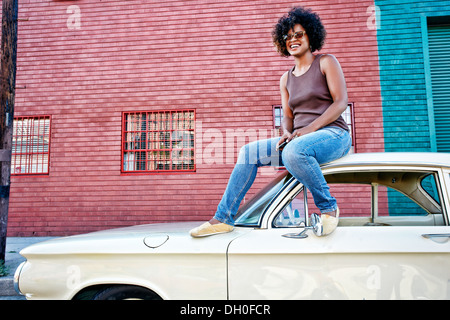 Mixed race woman sitting on vintage car Stock Photo