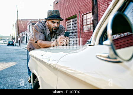 Hispanic man using cell phone on vintage car Stock Photo