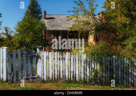 Photograph of a two story brick house surrounded by an unkempt yard and an old white picket fence Stock Photo