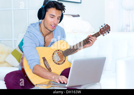 Mixed race teenager playing guitar and using laptop Stock Photo
