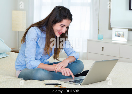 Hispanic woman using laptop on bed Stock Photo