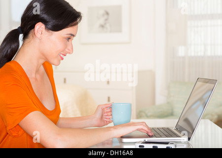 Mixed race woman drinking coffee and using laptop Stock Photo
