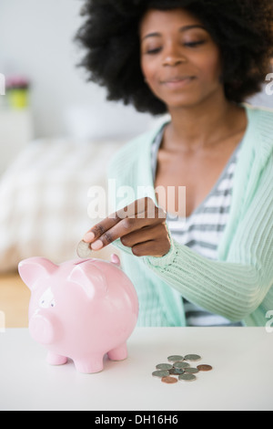 Mixed race woman putting coins in piggy bank Stock Photo