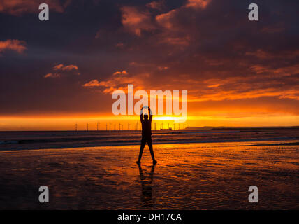 Jogger stretching on Seaton Carew beach at sunrise. Wind turbines in distance. Stock Photo