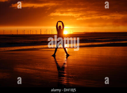 Jogger stretching on Seaton Carew beach at sunrise. Wind turbines in distance. Stock Photo