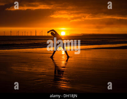 Jogger stretching on Seaton Carew beach at sunrise. Wind turbines in distance. Stock Photo