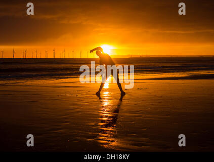 Jogger stretching on Seaton Carew beach at sunrise. Wind turbines in distance. Stock Photo