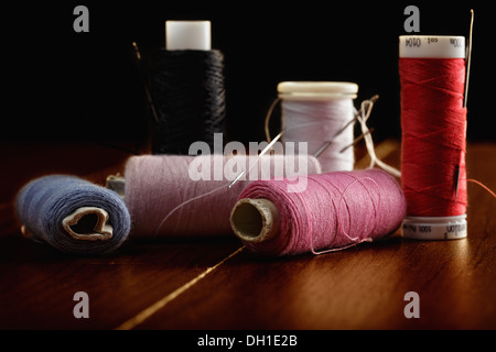 Spool of dark, black thread with needle and one metal thimble on