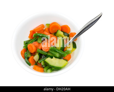 A white bowl filled with cooked zucchini, green beans and carrots in a butter sauce with a serving spoon. Stock Photo