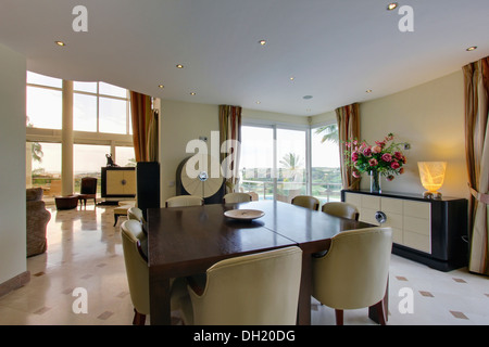 Cream leather upholstered chairs and polished table in dining area of large modern villa in Spain with lamp on sideboard Stock Photo