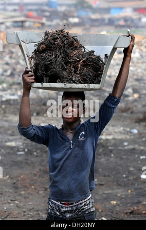 Teenage boy carries raw copper cables from burned computers, Agbogbloshie dump site in Accra, Ghana Stock Photo