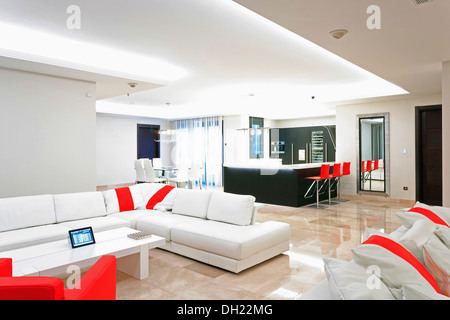 i-Pad on low table beside white sofa in large open-plan living area with red armchair in newly built villa in southern Spain Stock Photo
