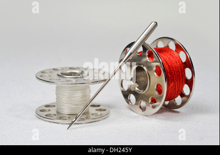 Sewing machine needles with yarn spools lying on white linen fabric Stock Photo