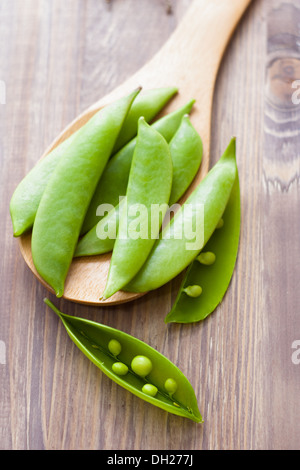 Pea pods on spoon, wooden background Stock Photo