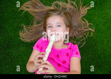 Blond kid children girl playing flute lying on grass backyard lawn Stock Photo