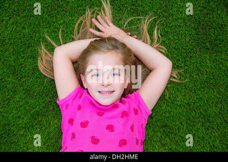 Beautiful blond kid children girl smiling relaxed lying on grass backyard lawn Stock Photo